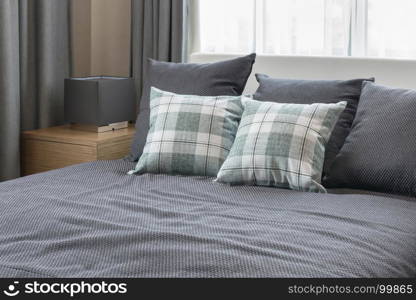 bedroom interior design with checked green pillows on grey bed and decorative table lamp.