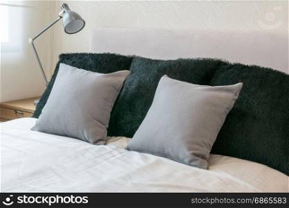 bedroom interior design with grey pillows on white bed and decorative table lamp.