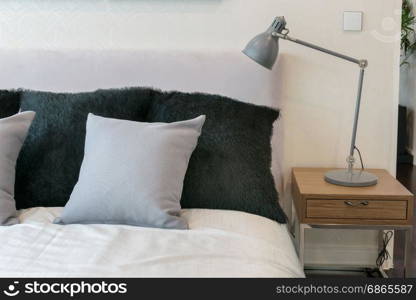 bedroom interior design with grey pillows on white bed and decorative table lamp.