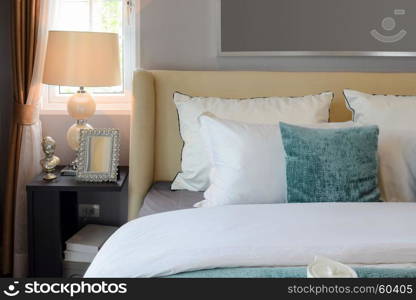 bedroom interior design with white and green pillows on white bed and decorative table lamp.