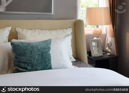 bedroom interior design with white and green pillows on white bed and decorative table lamp.