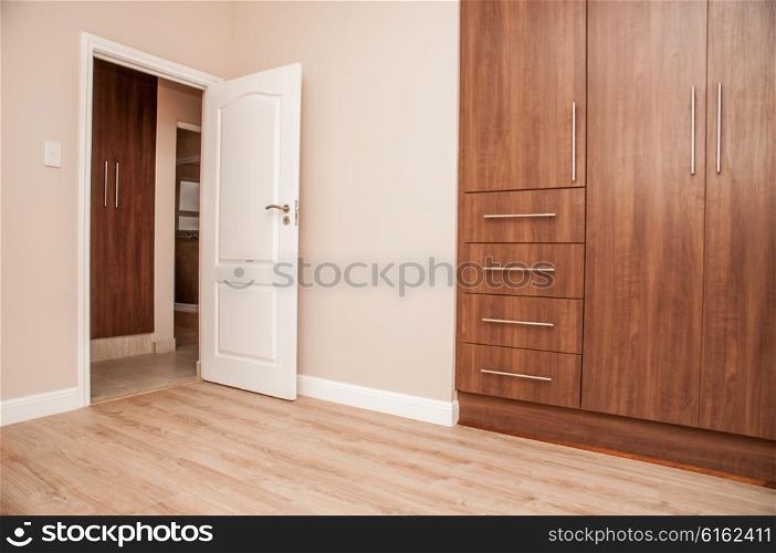 Bedroom of New House with build in cupboards, and laminated floor, as viewed towards the open door to the bedroom.