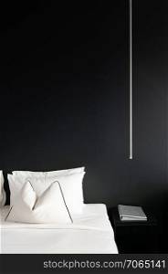 Bedroom with black concrete wall white bed, white pillows and simple design side table, lamp. Modern urban interior with black and white colours tone