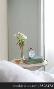 Bedside table with cut flower and alarm clock