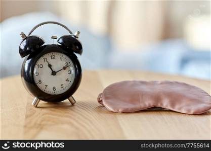 bedtime and morning concept - close up of alarm clock and eye sleeping mask on night table at home. alarm clock and eye sleeping mask on table at home