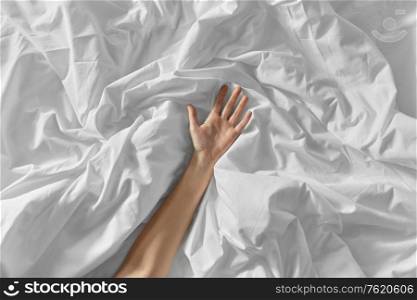 bedtime, sex and rest concept - hand of woman lying on rumpled bed sheet. hand of woman lying on rumpled bed sheet