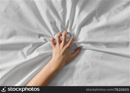 bedtime, sex and rest concept - hand of woman squeezing white bed sheet. hand of woman squeezing white bed sheet