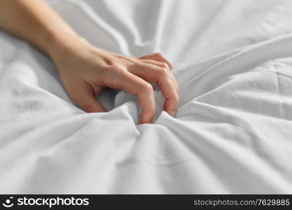 bedtime, sex and rest concept - hand of woman squeezing white bed sheet. hand of woman squeezing white bed sheet