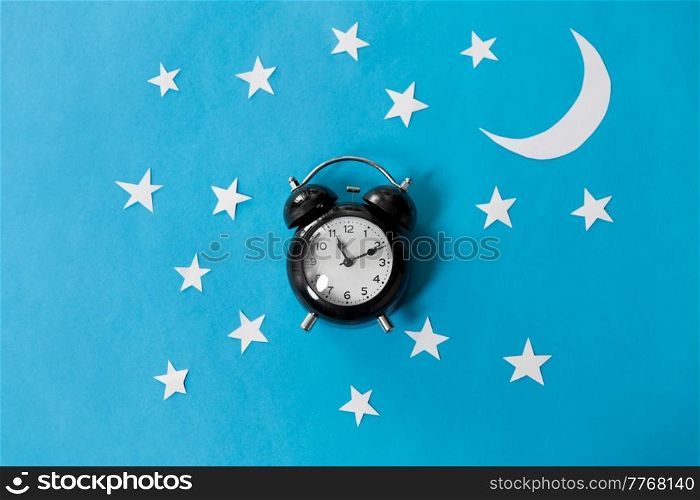 bedtime, sleeping and night time concept - close up of alarm clock showing midnight hour on blue paper background with moon and stars. alarm clock on blue night background