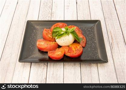 beef cheese burrata with diced tomatoes, basil leaves, pepper and salt on a black plate