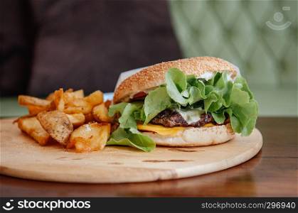 Beef cheeseburger, fried potato chunks with ranch dipping sauce on wood plate close up shot