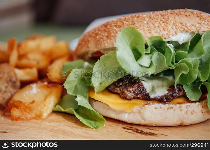 Beef cheeseburger, fried potato chunks with ranch dipping sauce on wood plate close up shot