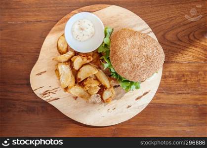 Beef cheeseburger, fried potato chunks with ranch dipping sauce on wood plate top view shot
