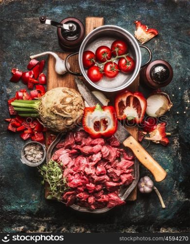 Beef goulash of young bulls with vegetables and cooking ingredients , preparation on cutting board and dark rustic background , top view composing
