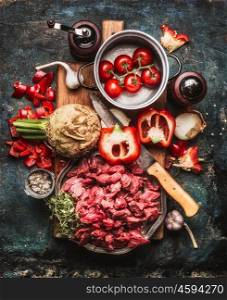 Beef goulash of young bulls with vegetables and cooking ingredients , preparation on cutting board and dark rustic background , top view composing