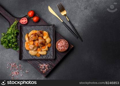 Beef meat and vegetables stew on a black plate with roasted potatoes. Dark background. Copy space. Beef meat and vegetables stew on a black plate with roasted potatoes