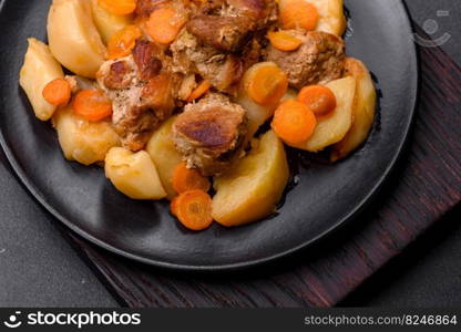 Beef meat and vegetables stew on a black plate with roasted potatoes. Dark background. Copy space. Beef meat and vegetables stew on a black plate with roasted potatoes