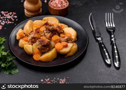 Beef meat and vegetables stew on a black plate with roasted potatoes. Dark background. Copy space. Beef meat and vegetables stew on a black plate with roasted potatoes