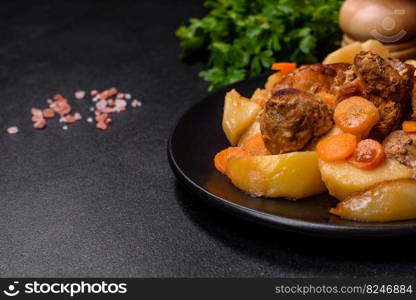 Beef meat and vegetables stew on a black plate with roasted potatoes. Dark background. Copy space. Beef meat and vegetables stew on a black plate with roasted potatoes