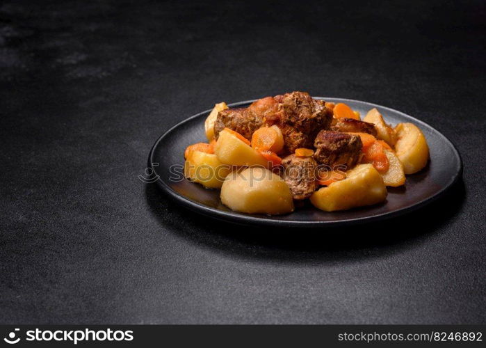 Beef meat and vegetables stew on a black plate with roasted potatoes. Dark background. Copy space. Beef meat and vegetables stew on a black plate with roasted potatoes