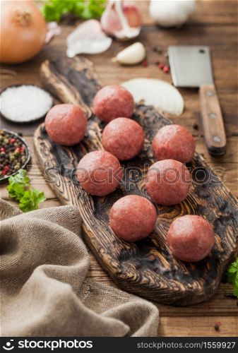 Beef meatballs on wooden board with pepper, salt and garlic with onion, parsley and dill on wood background.