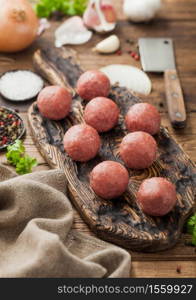 Beef meatballs on wooden board with pepper, salt and garlic with onion, parsley and dill on wood background.