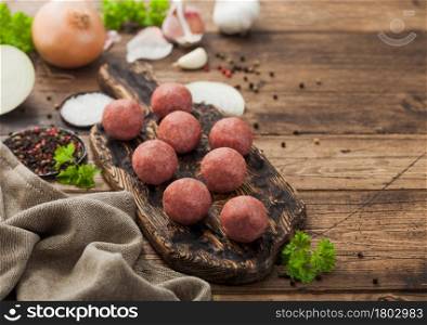 Beef meatballs on wooden board with pepper, salt and garlic with onion, parsley and dill on wood background.