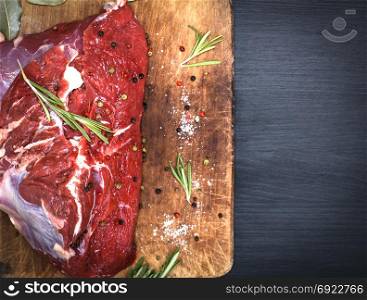 Beef piece of meat on a brown kitchen board, empty space on the right