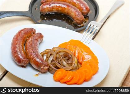 beef sausages cooked on iron skillet with carrot and onion