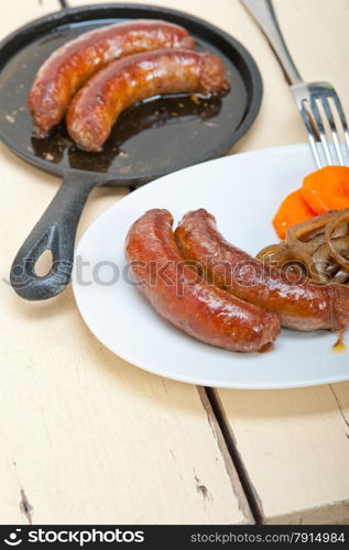 beef sausages cooked on iron skillet with carrot and onion