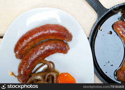 beef sausages cooked on iron skillet with carrot and onion