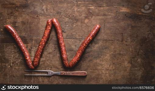 Beef sausages for grill or bbq with meet fork on rustic wooden background, top view. Place for your design, text or recipes. Letter W make with sausages