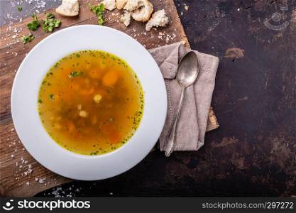 Beef soup with carrots and herbs on a dark background, top view