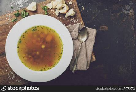 Beef soup with carrots and herbs on a dark background, top view