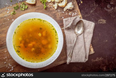 Beef soup with carrots and herbs on a dark background, top view