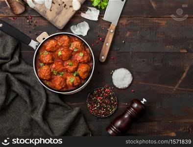 Beef spicy meatballs in tomato sauce with pepper, garlic and parsley with onion and cleaver on dark wooden background. Space for text