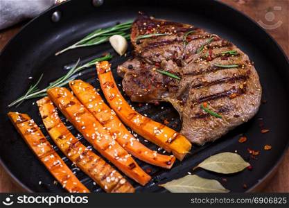 Beef stack with spices cooked with carrot sticks on a black round frying pan, close up