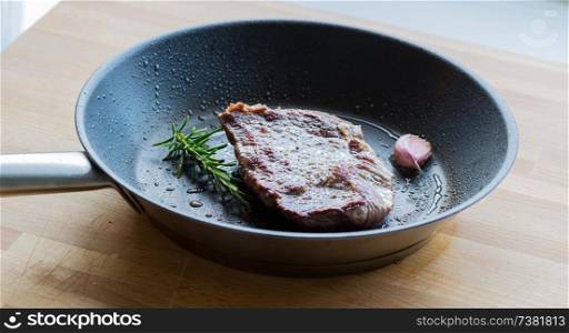 Beef steak is fried in a pan with rosemary and garlic.. Beef steak is fried in a pan with rosemary and garlic