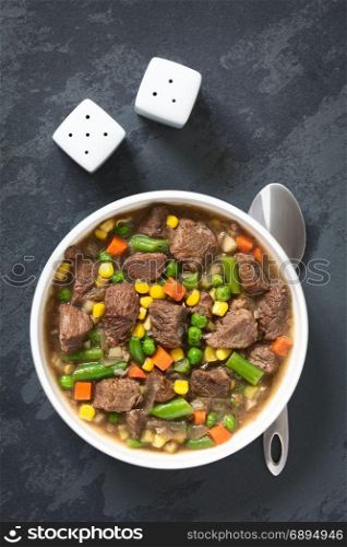 Beef stew or soup with colorful summer vegetables (pea, carrot, sweet corn, green bean, onion) in bowl, photographed overhead on slate with natural light. Beef Stew or Soup with Vegetables