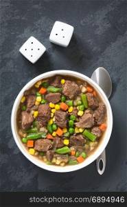 Beef stew or soup with colorful summer vegetables (pea, carrot, sweet corn, green bean, onion) in bowl, photographed overhead on slate with natural light. Beef Stew or Soup with Vegetables
