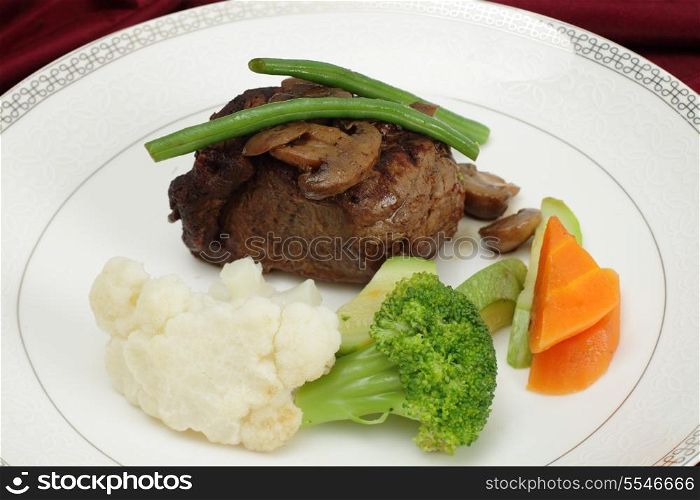 Beef tournedos (tenderloin fillet steak) served with mushrooms, steamed beans, courgettes, cauliflower, carrot and broccoli, a minimalist modern take on a traditional favourite.