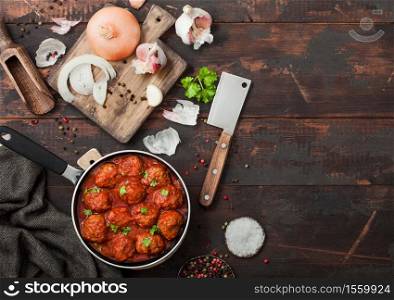 Beef traditional meatballs in tomato sauce in frying pan with pepper, garlic and parsley with onion and cleaver on wooden board. Top view