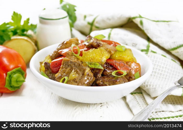 Beef with oranges, bell pepper and ginger root in a bowl, towel and a fork on wooden board background