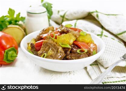 Beef with oranges, bell pepper and ginger root in a bowl, towel and a fork on wooden board background