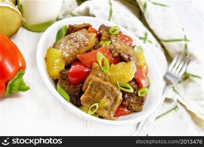 Beef with oranges, bell pepper and ginger root in bowl, a napkin and a fork on the background of light wooden board