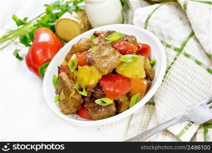 Beef with oranges, bell peppers and ginger root in bowl, a napkin and a fork on white wooden board background
