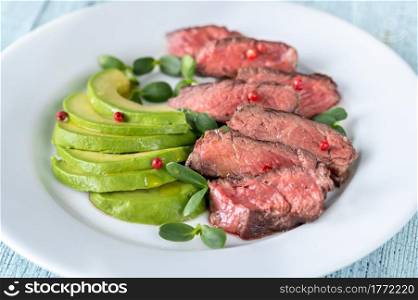 Beefsteak decorated with red peppercorn and garnished with slices of avocado