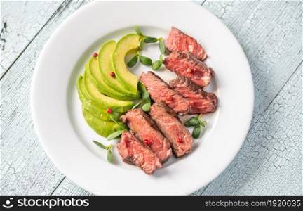 Beefsteak decorated with red peppercorn and garnished with slices of avocado