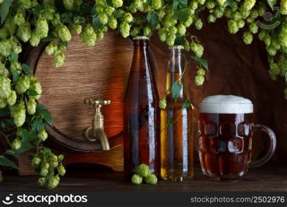 Beer bottles with glass of beer and barrel with fresh hops frame still-life