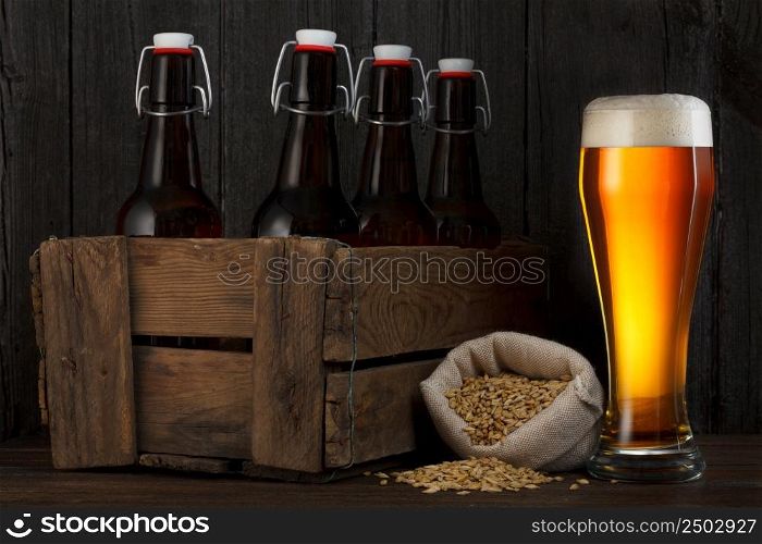 Beer glass and beer barley in bag with wooden box full of bottles on table